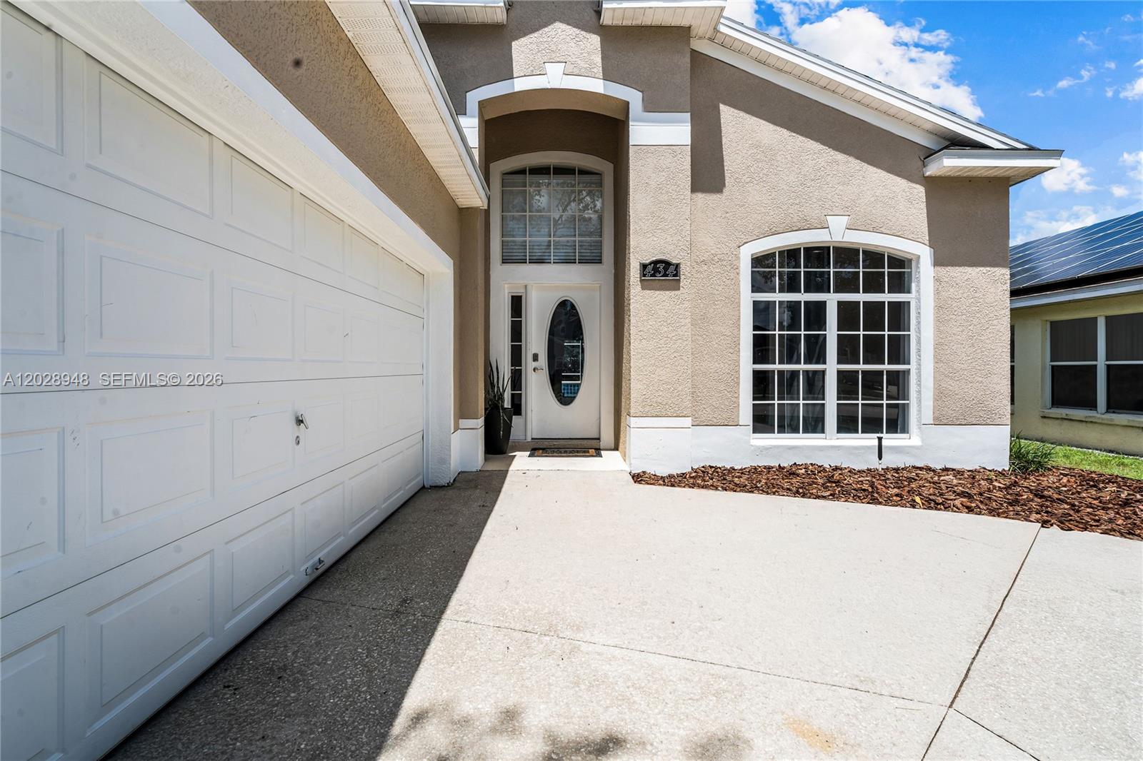 The exterior of a beige house features a white garage door and a front entrance — 434 Castlemain, Davenport FL 33897, DAVENPORT, FL