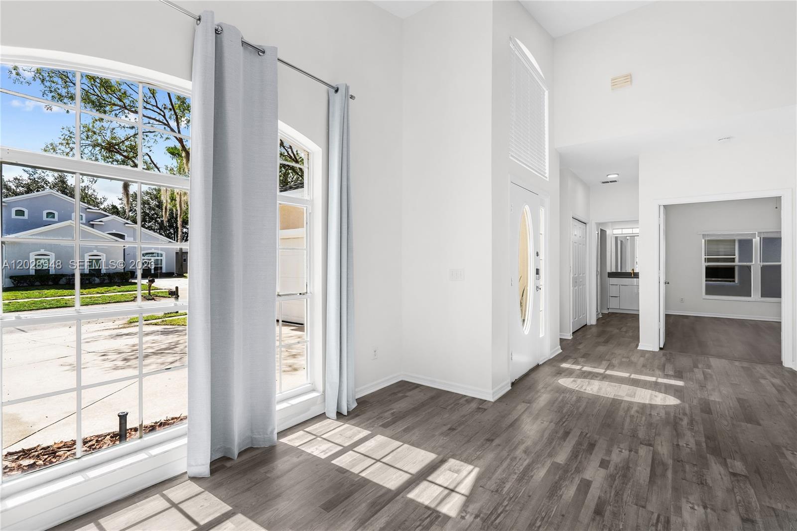 A bright entryway features high ceilings, gray wood-look flooring, and large windows with light curtains — 434 Castlemain, Davenport FL 33897, DAVENPORT, FL