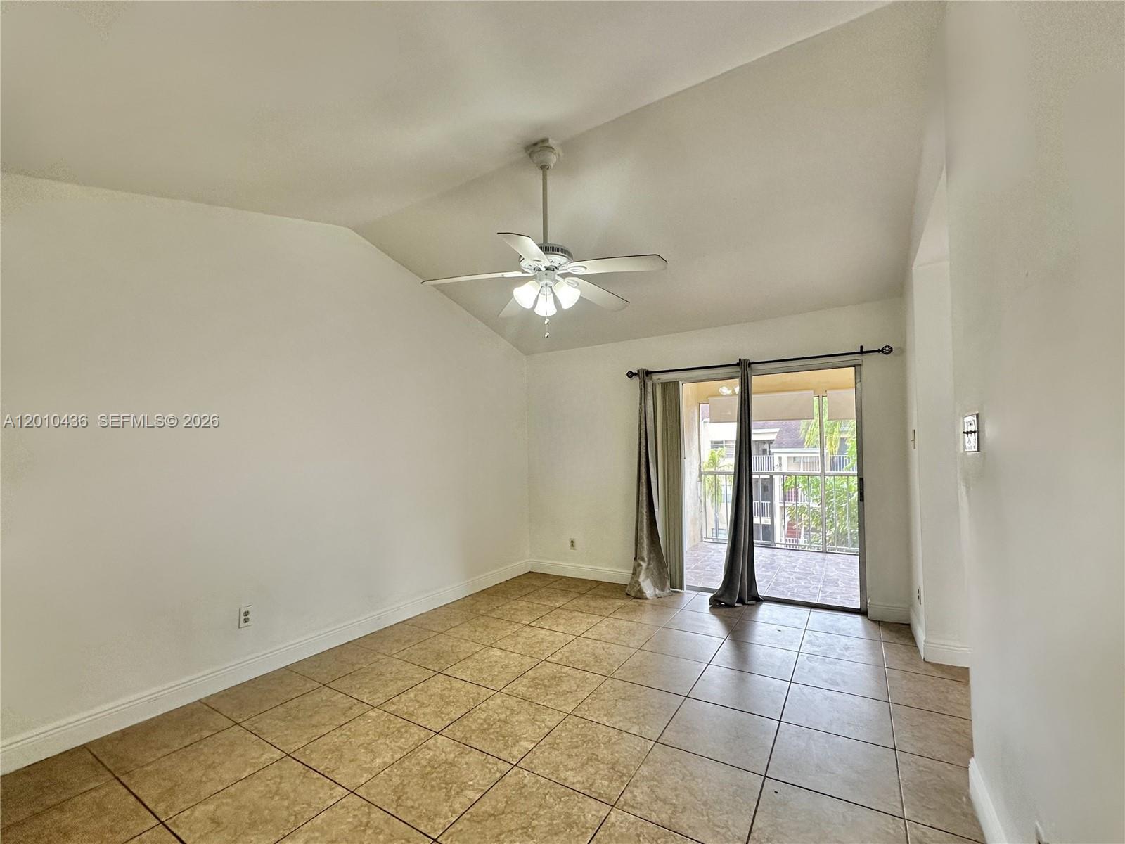 An empty room features vaulted ceilings, a ceiling fan, tile flooring, and a sliding glass door — 15300 SW 106th Ter # 506, Miami FL 33196, MIAMI, FL