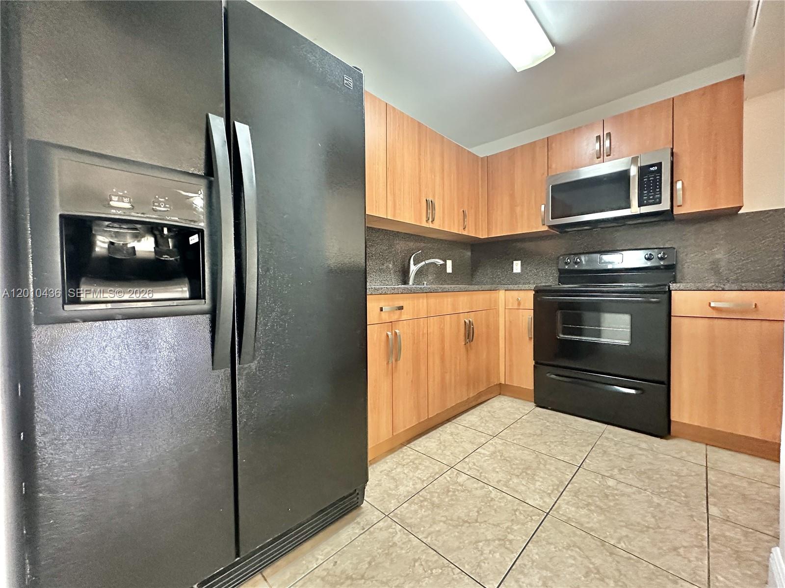 A kitchen features light wood cabinets, black appliances, and tiled flooring — 15300 SW 106th Ter # 506, Miami FL 33196, MIAMI, FL