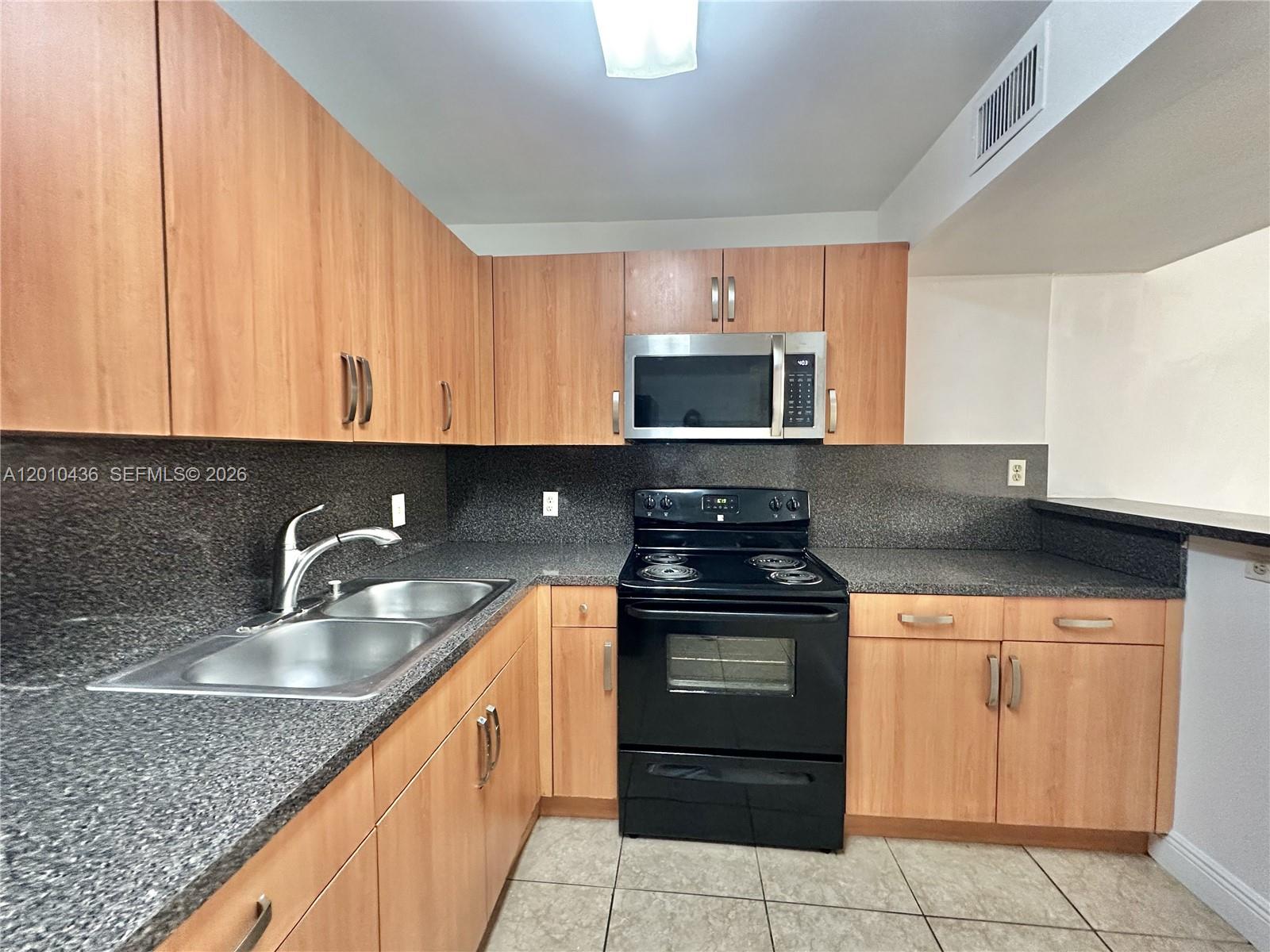 A kitchen features light wood cabinets, dark granite countertops, and black appliances — 15300 SW 106th Ter # 506, Miami FL 33196, MIAMI, FL