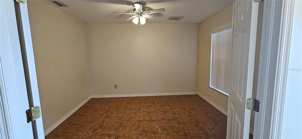 An empty room features tan tile flooring, a ceiling fan, and white walls — 3007 SW SANTA BARBARA PLACE, CAPE CORAL, FL