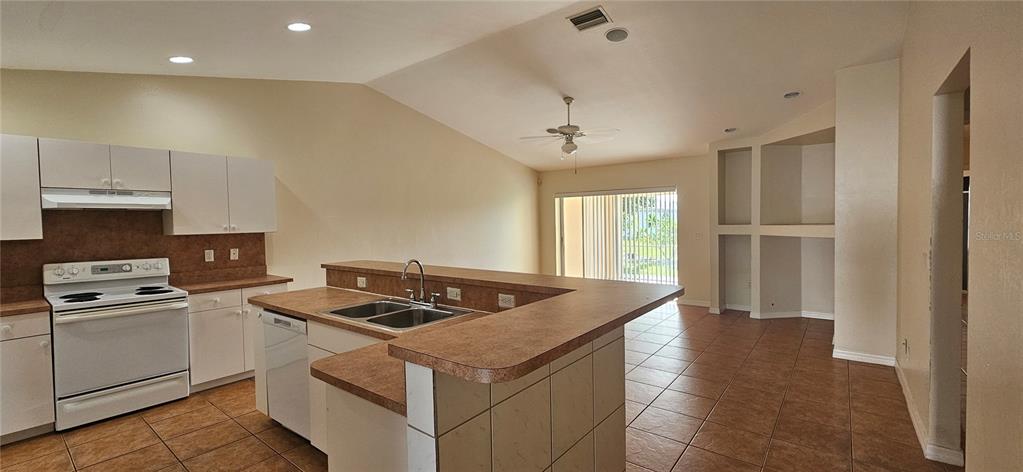 A kitchen with white cabinets, laminate countertops, and tile flooring opens to a living area — 3007 SW SANTA BARBARA PLACE, CAPE CORAL, FL