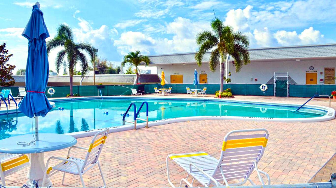 A swimming pool with lounge chairs and umbrellas sits in front of a low-rise building — 2920 Cynthia Lane # 202, FL 33461, FL