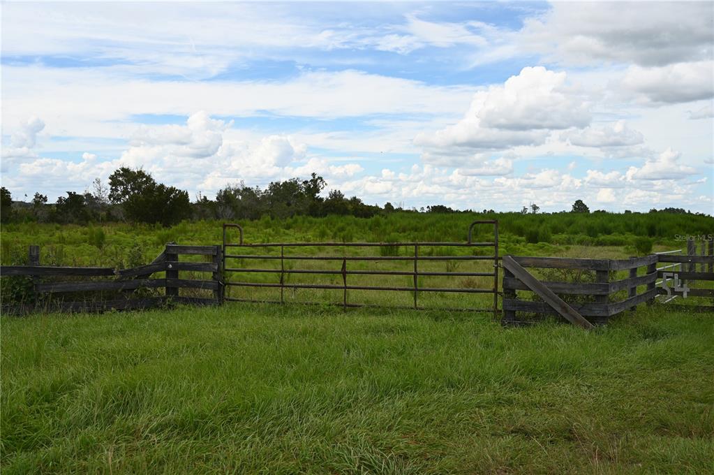 A metal gate sits between sections of wooden fencing in a grassy, open field — COUNTY LINE ROAD E, FORT MEADE, FL