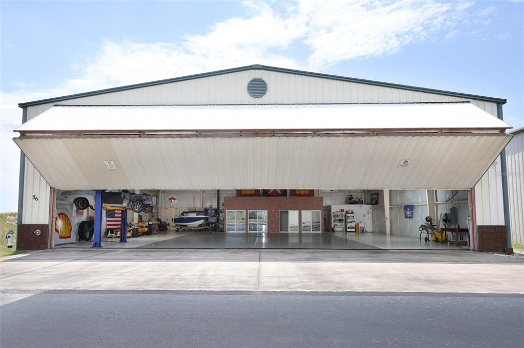 A large hangar with an open bi-fold door, concrete floor, and a vehicle lift inside — 1312 APOPKA AIRPORT ROAD, APOPKA, FL