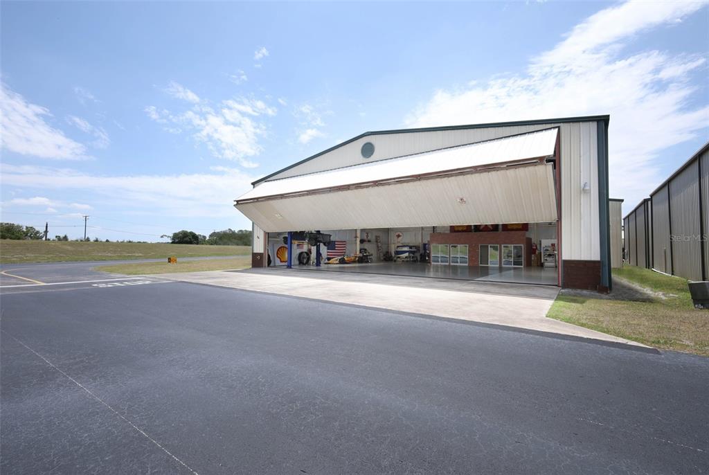 An exterior view of a large metal hangar with a wide, open bi-fold door — 1312 APOPKA AIRPORT ROAD, APOPKA, FL