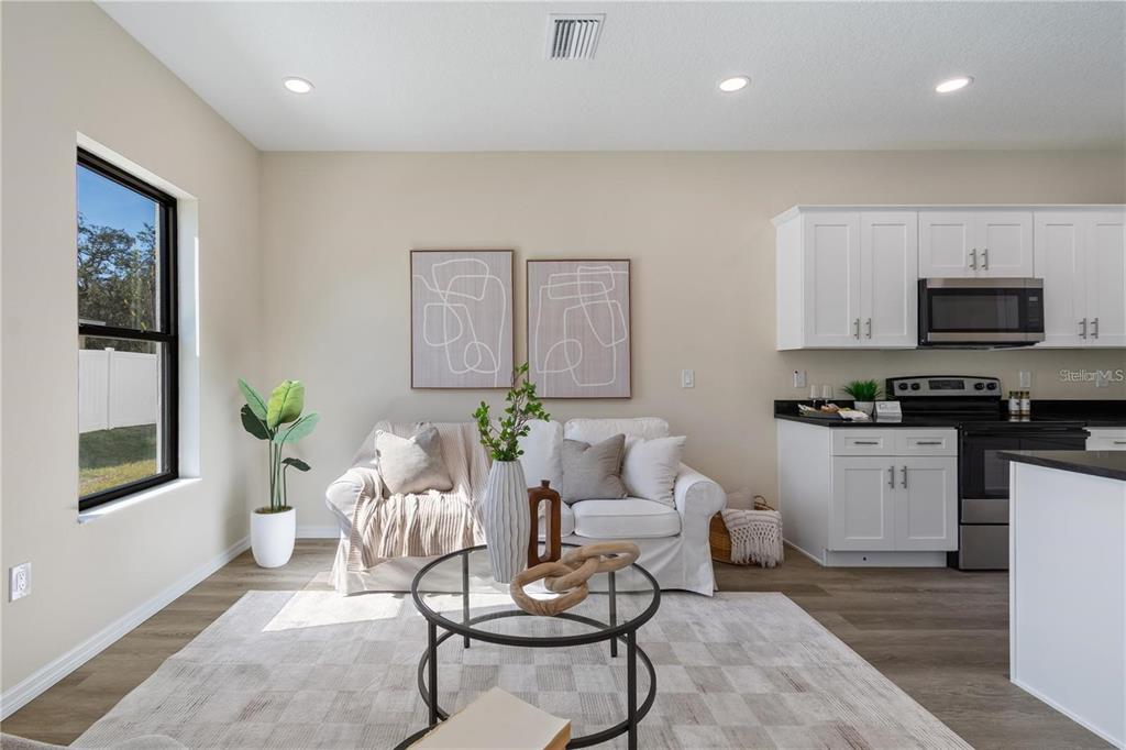 A living room with a white sofa, round coffee table, and adjacent kitchen with white cabinets — 4367 CAMBIO GARDENS COURT, TAMPA, FL