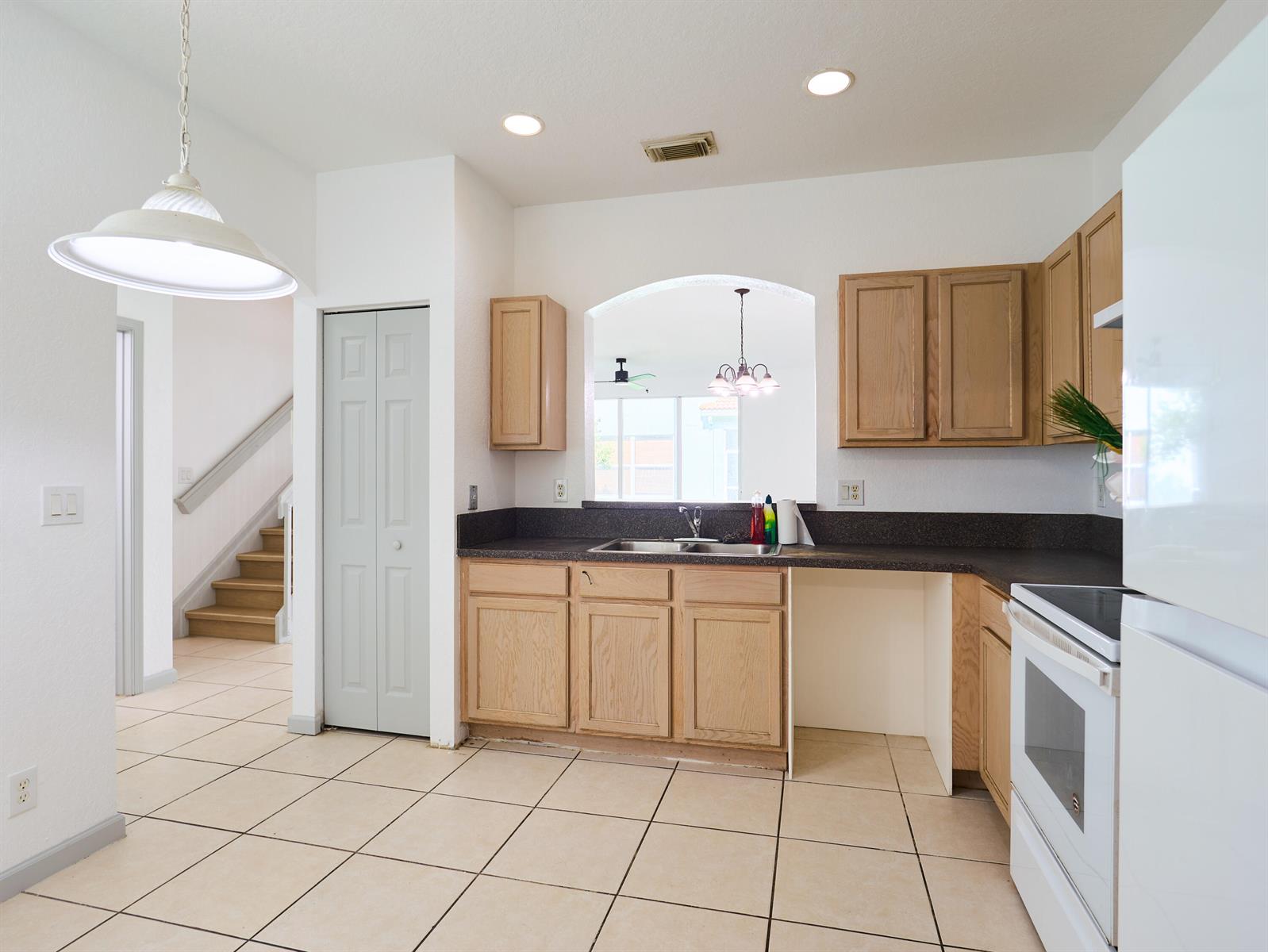 A kitchen features light wood cabinets, dark countertops, white appliances, and tile flooring — 2052 Oakhurst Way, Riviera Beach FL 33404, RIVIERA BEACH, FL