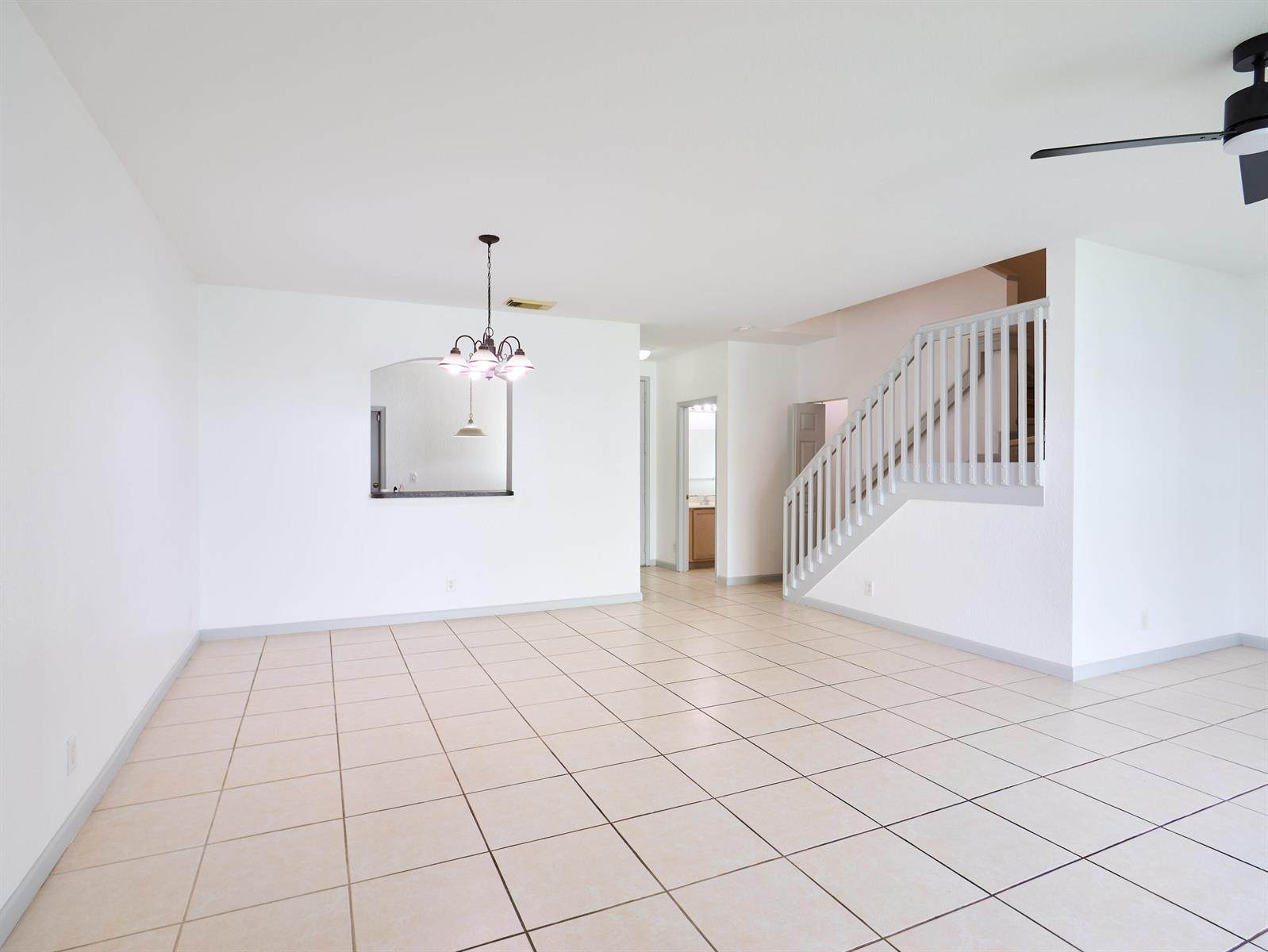 An empty room with light tile flooring, a dining chandelier, and a staircase with railings — 2052 Oakhurst Way, Riviera Beach FL 33404, RIVIERA BEACH, FL