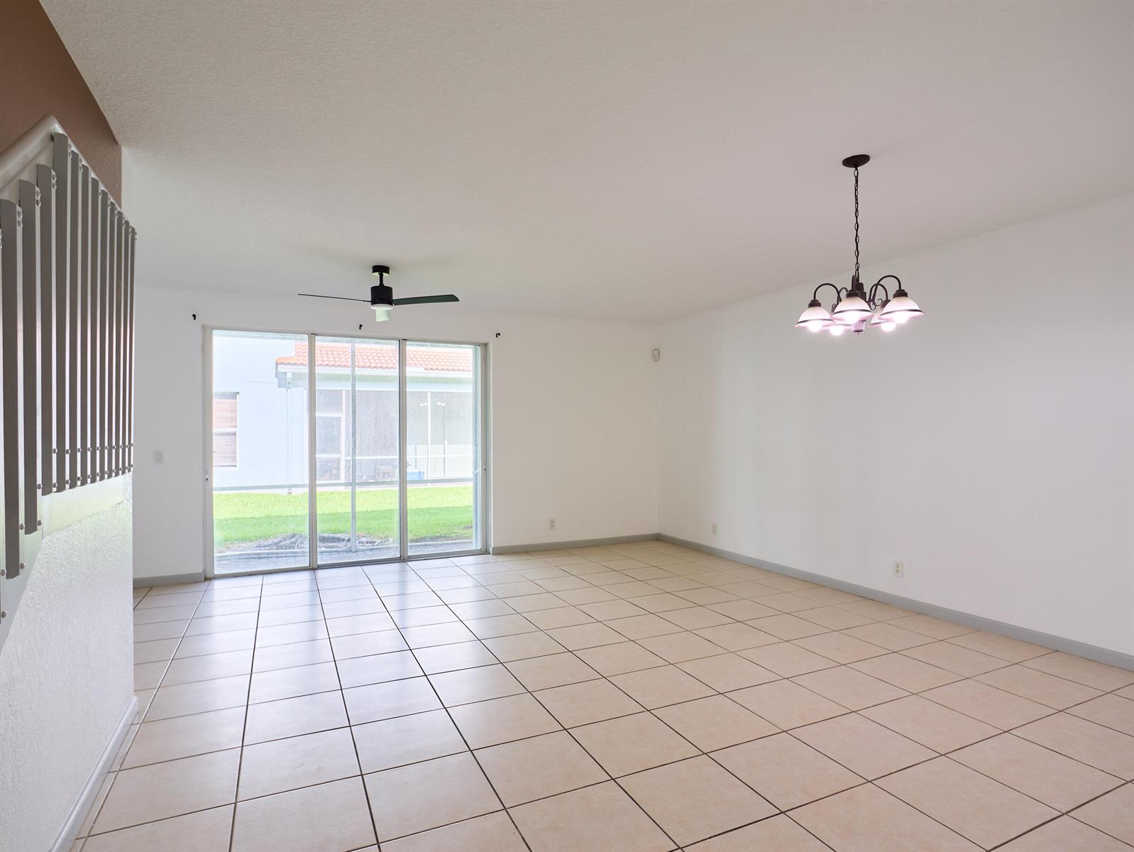An empty living room features beige tile flooring, a ceiling fan, and a dining chandelier — 2052 Oakhurst Way, Riviera Beach FL 33404, RIVIERA BEACH, FL