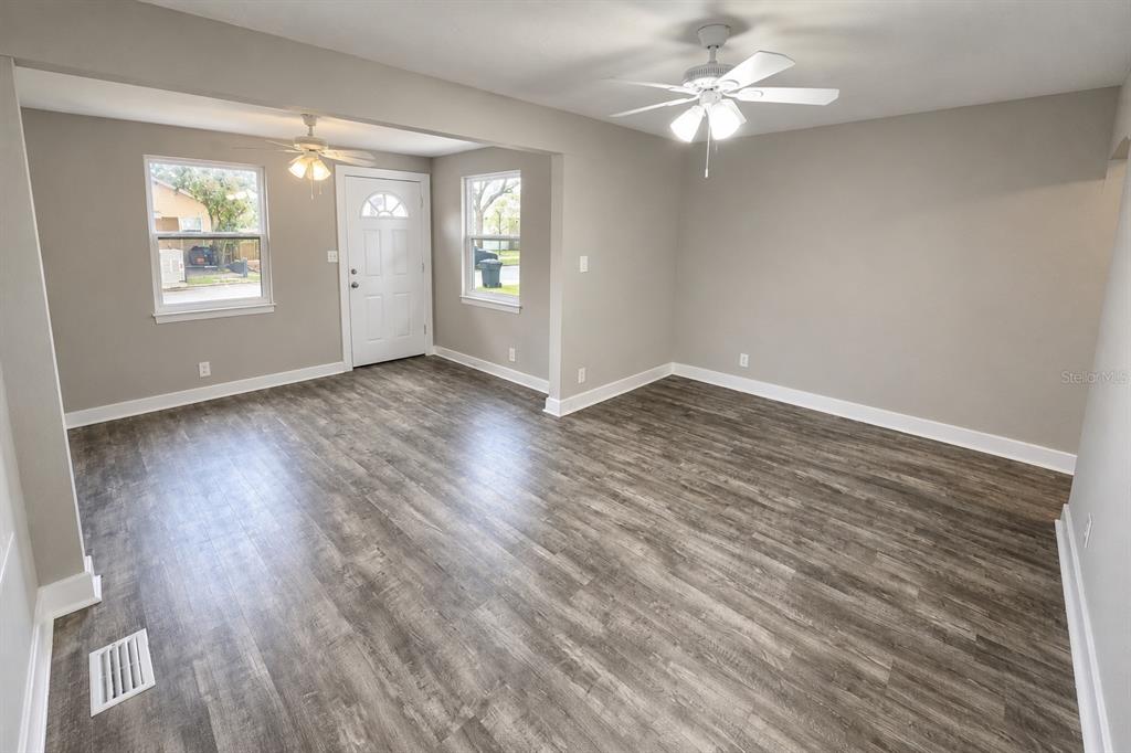 An empty living room features gray walls, wood-look flooring, two ceiling fans, and a front door — 657 15TH AVENUE S, ST PETERSBURG, FL