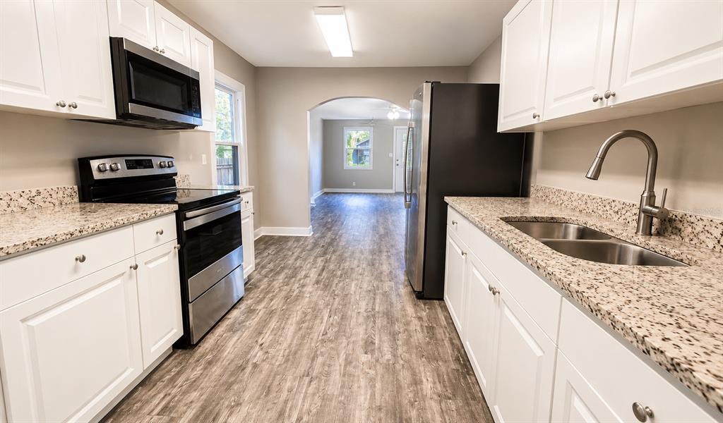A kitchen features white cabinets, granite countertops, stainless steel appliances, and wood-look flooring — 657 15TH AVENUE S, ST PETERSBURG, FL