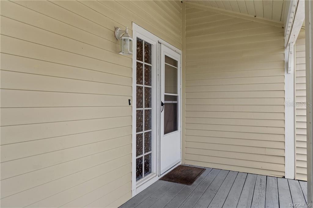 A covered porch features light-colored horizontal siding, a white storm door, and a wooden deck — 1304 CYPRESS COVE COURT, INVERNESS, FL