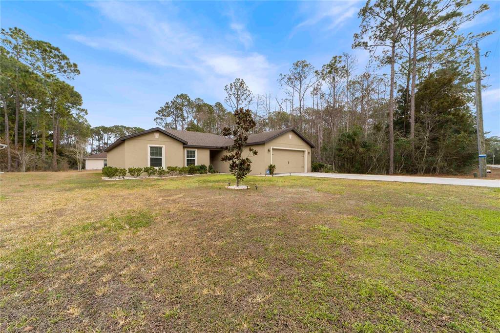 A single-story tan house with a two-car garage sits on a large, grassy lot — 50 ULLIAN TRAIL, PALM COAST, FL