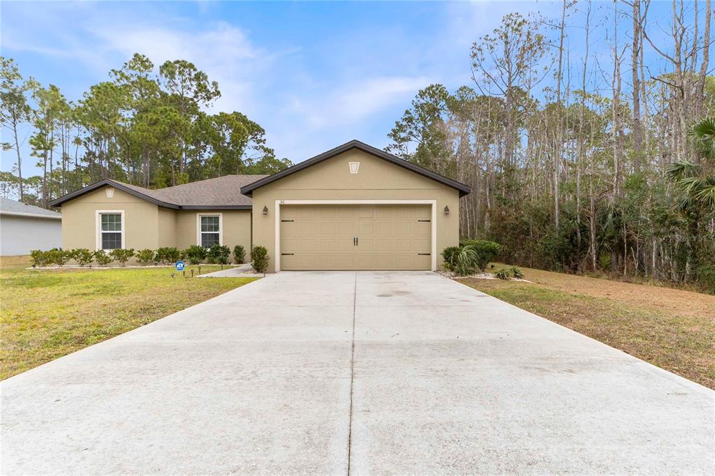 A single-story house with a tan stucco exterior, a two-car garage, and a concrete driveway — 50 ULLIAN TRAIL, PALM COAST, FL