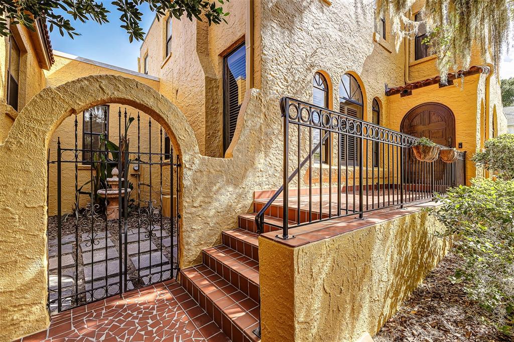 A yellow stucco house exterior features a gated courtyard, arched windows, and a tiled staircase — 327 MIRAMAR ROAD, LAKELAND, FL