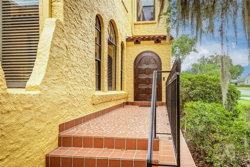 A yellow stucco house exterior features a tiled porch, arched windows, and a wooden door — 327 MIRAMAR ROAD, LAKELAND, FL