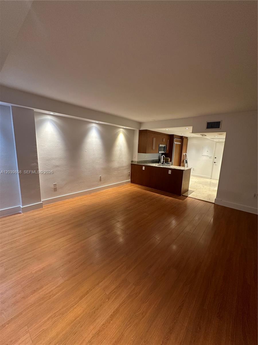 This room features wood-look flooring, recessed lighting, and an open kitchen with dark cabinetry — BAL HARBOUR, FL