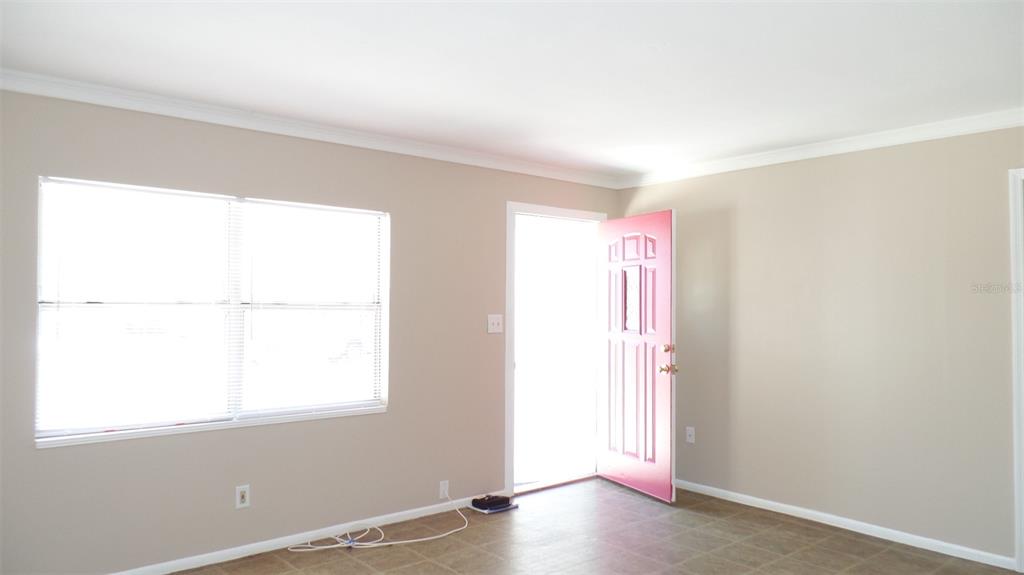 A room with beige walls, tile flooring, a large window, and a bright pink front door — 4935 EMERSON AVENUE S, ST PETERSBURG, FL