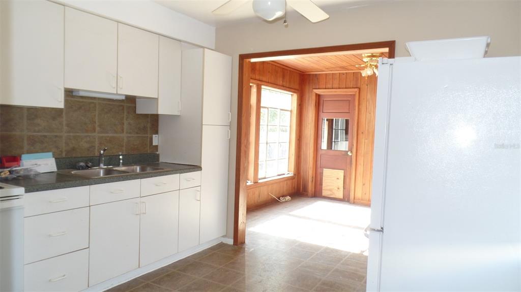 A kitchen with white cabinets and a dark countertop leads into a wood-paneled room — 4935 EMERSON AVENUE S, ST PETERSBURG, FL
