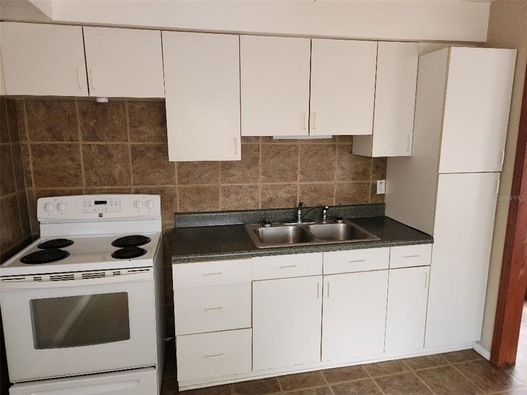A kitchen features white cabinets, a white electric stove, a double sink, and tiled backsplash — 4935 EMERSON AVENUE S, ST PETERSBURG, FL