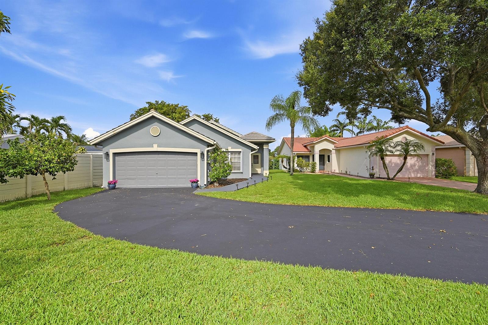 A gray house with a two-car garage and a curved asphalt driveway sits on grass — 12445 SW 7th Place, Davie FL 33325, DAVIE, FL