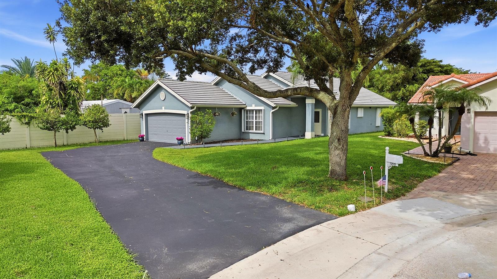 A blue single-story house with a gray roof, asphalt driveway, and large front yard tree — 12445 SW 7th Place, Davie FL 33325, DAVIE, FL