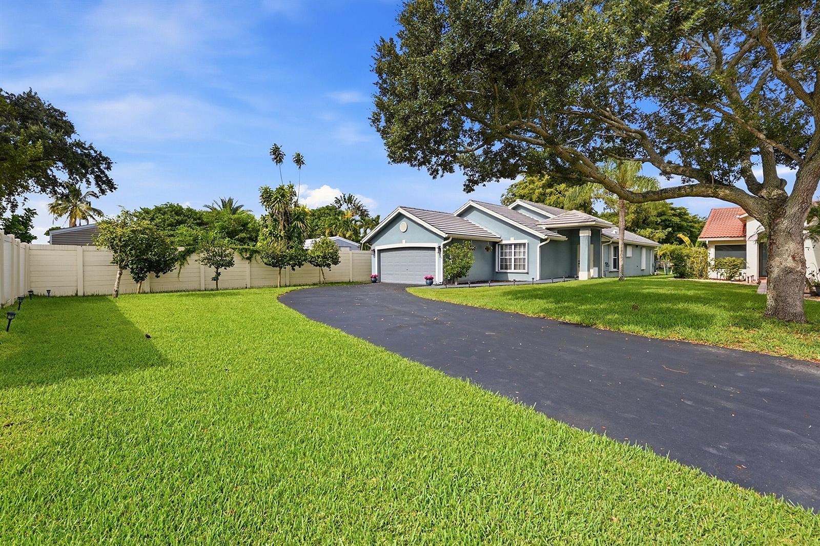 A blue single-story house with a curved asphalt driveway and a large tree in front — 12445 SW 7th Place, Davie FL 33325, DAVIE, FL