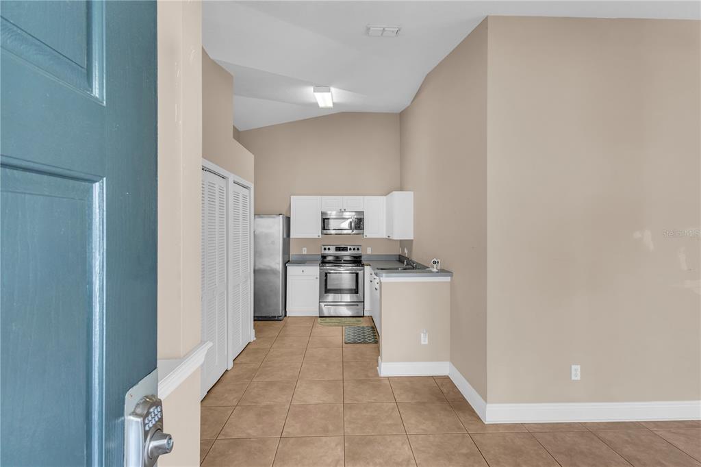 A kitchen with stainless steel appliances, white cabinets, and tan tile flooring — 8810 GRAND PALMS CIRCLE UNIT B, KISSIMMEE, FL