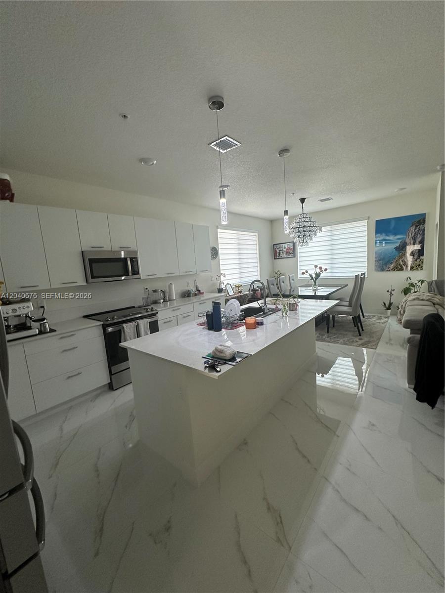 A modern kitchen features white cabinetry, a central island, and white marble-patterned tile flooring — 8001 NW 41st St # 113, Doral FL 33166, DORAL, FL