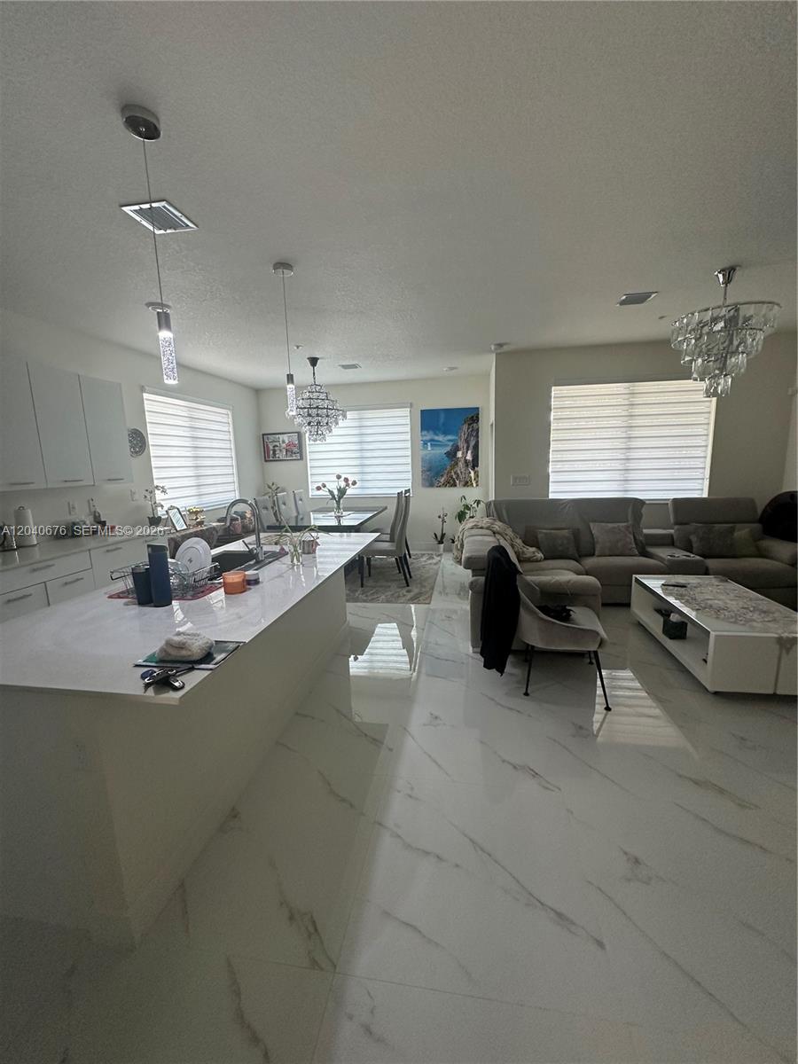 An open-concept kitchen and living area features white marble floors, white cabinetry, and crystal chandeliers — 8001 NW 41st St # 113, Doral FL 33166, DORAL, FL