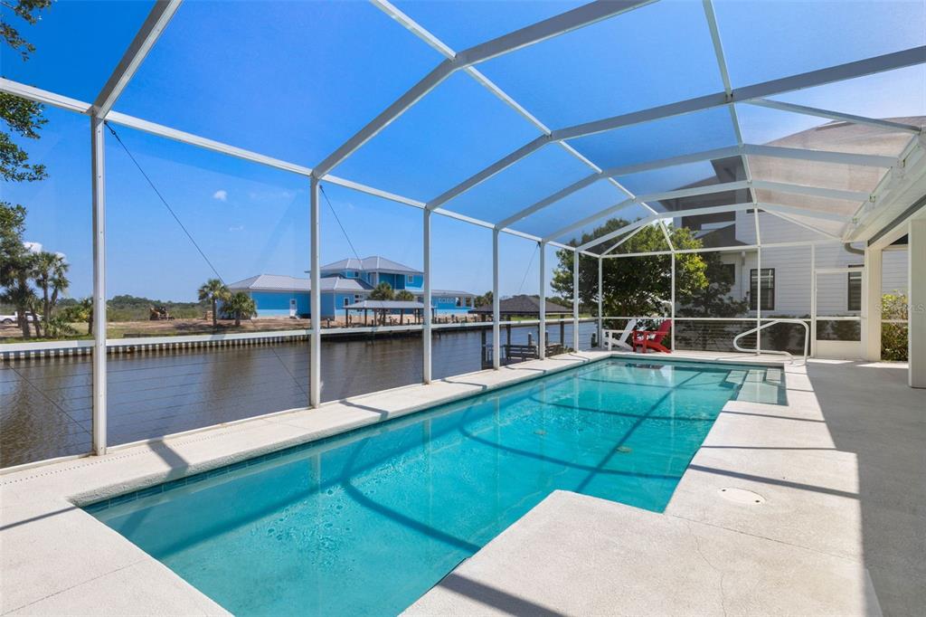 A rectangular swimming pool sits inside a screened-in lanai overlooking a canal and neighboring houses — 127 SEASIDE POINT, FLAGLER BEACH, FL