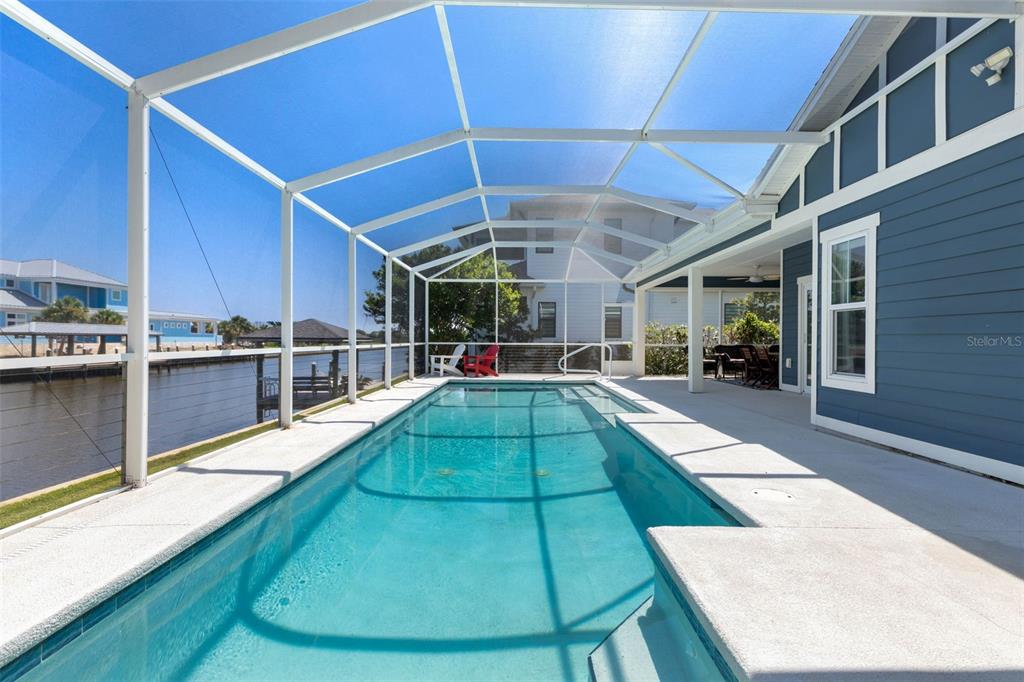 A rectangular swimming pool is enclosed by a screened lanai next to a blue house — 127 SEASIDE POINT, FLAGLER BEACH, FL