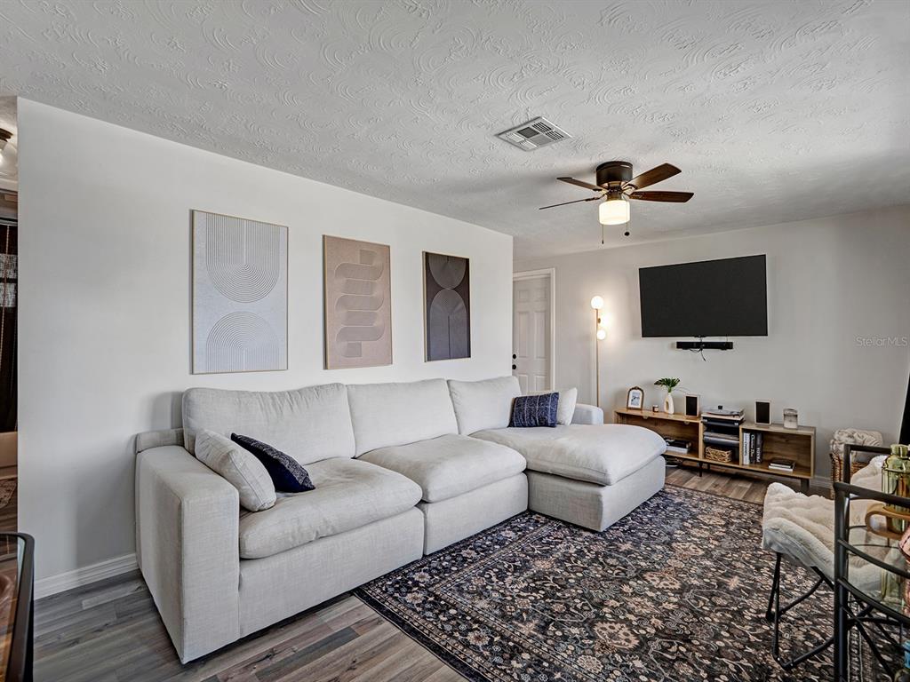 A living room features a light-colored sectional sofa, a patterned area rug, and wall-mounted television — 2603 SOCIETY DRIVE, HOLIDAY, FL