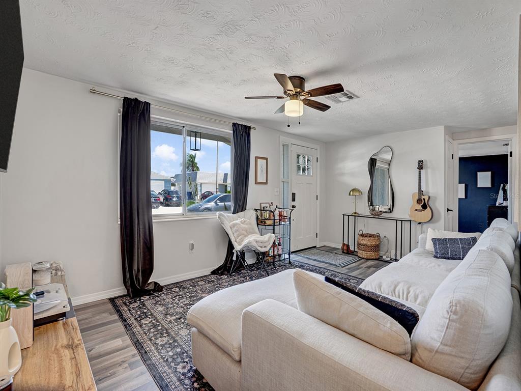 A living room features a white sectional sofa, a dark patterned rug, and a ceiling fan — 2603 SOCIETY DRIVE, HOLIDAY, FL