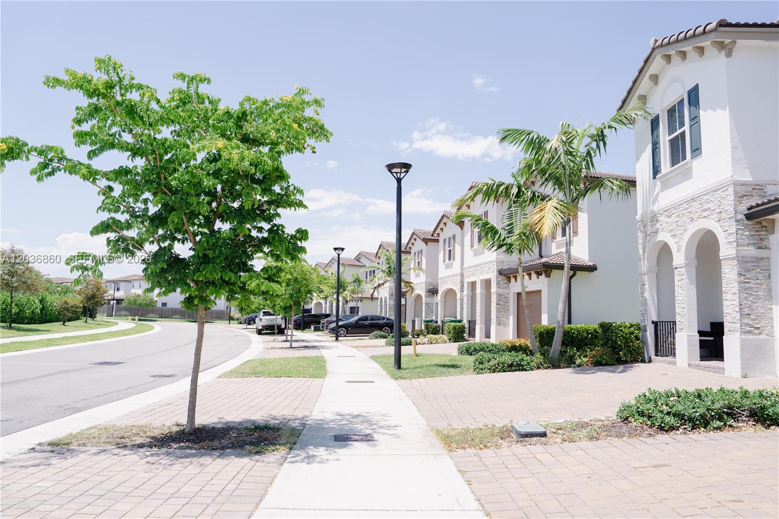 A row of two-story townhouses with paved driveways and palm trees lines a suburban street — 12779 NW 24th Ave # 0, Miami FL 33167, MIAMI, FL