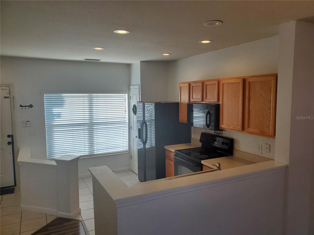 A kitchen features light wood cabinets, black appliances, and a partial wall overlooking the area — 4480 SW 49TH AVENUE, OCALA, FL