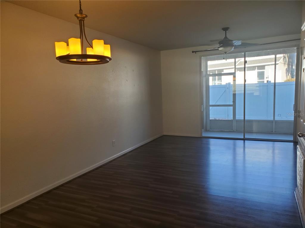 An empty room with dark wood-look flooring, a hanging light fixture, and a sliding glass door — 4480 SW 49TH AVENUE, OCALA, FL