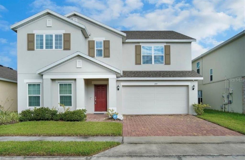 A two-story suburban house with a red front door, a garage, and a paved driveway — 244 HAMLET LOOP, DAVENPORT, FL