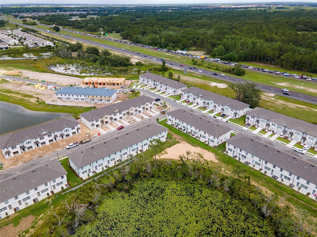 An aerial view shows multiple rows of townhouses near a highway and a pond — 1038 PLANTATION LANE, DAVENPORT, FL
