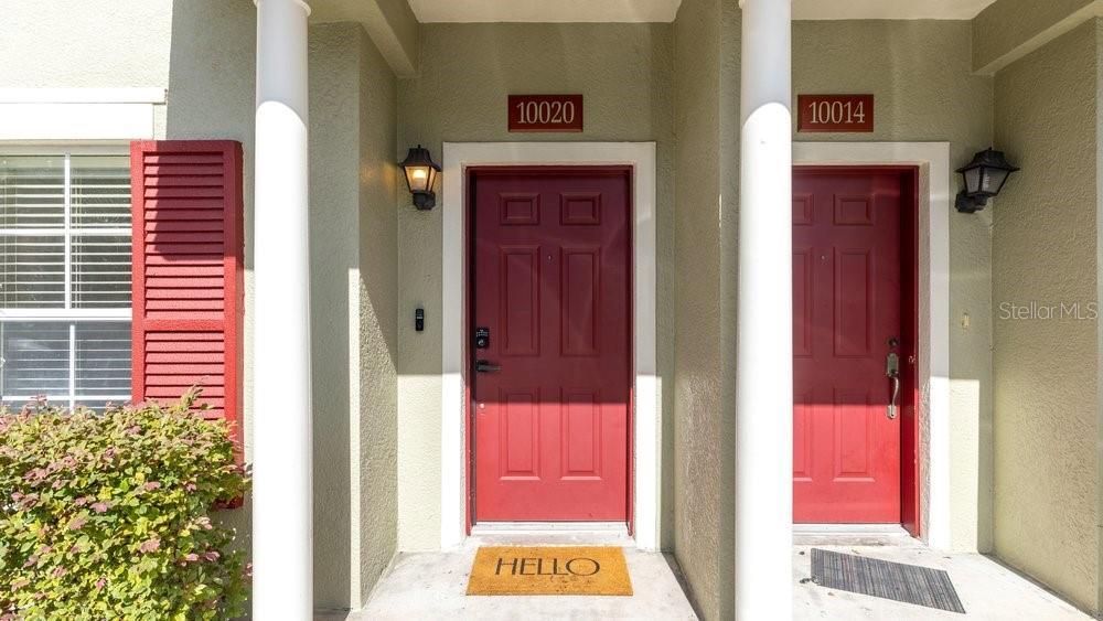Two red front doors with house numbers are positioned between white columns on a porch — 10020 REGENT PARK DRIVE UNIT 2405, ORLANDO, FL