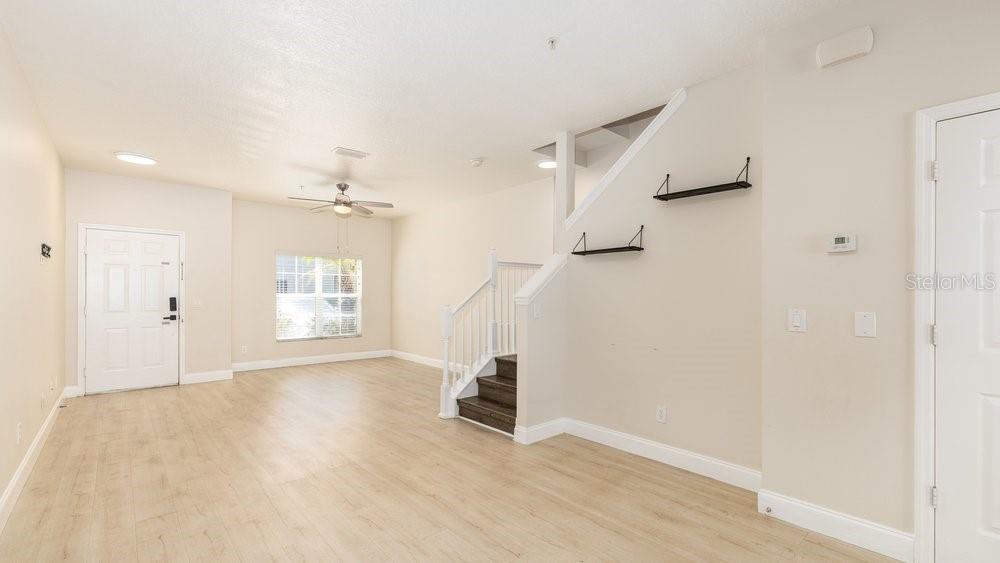 An open-concept living room features light wood-look flooring, a staircase, and two wall-mounted shelves — 10020 REGENT PARK DRIVE UNIT 2405, ORLANDO, FL