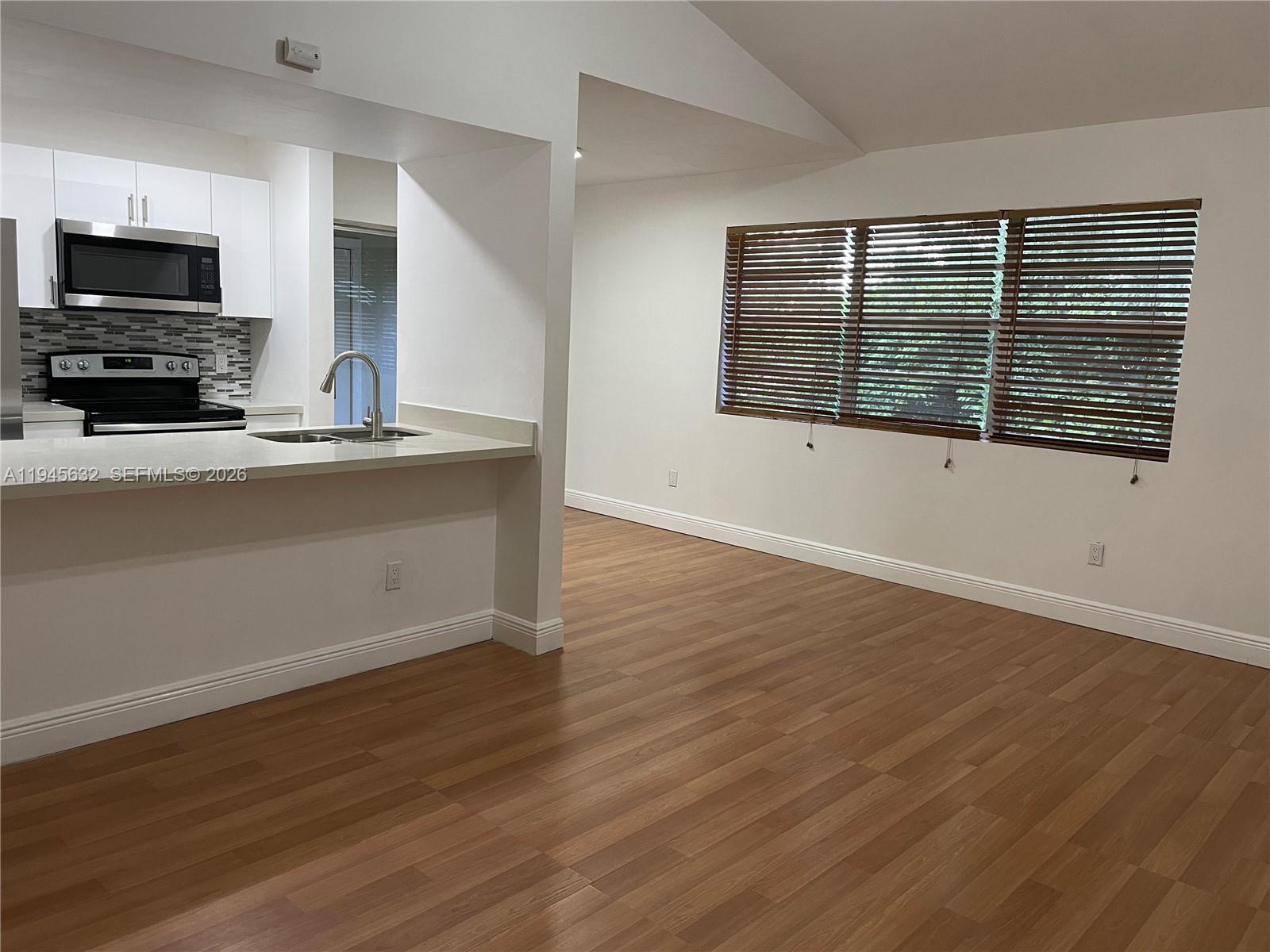 A kitchen with white cabinets and stainless steel appliances opens into a living area — 15325 SW 106th Ter # 618, Miami FL 33196, MIAMI, FL