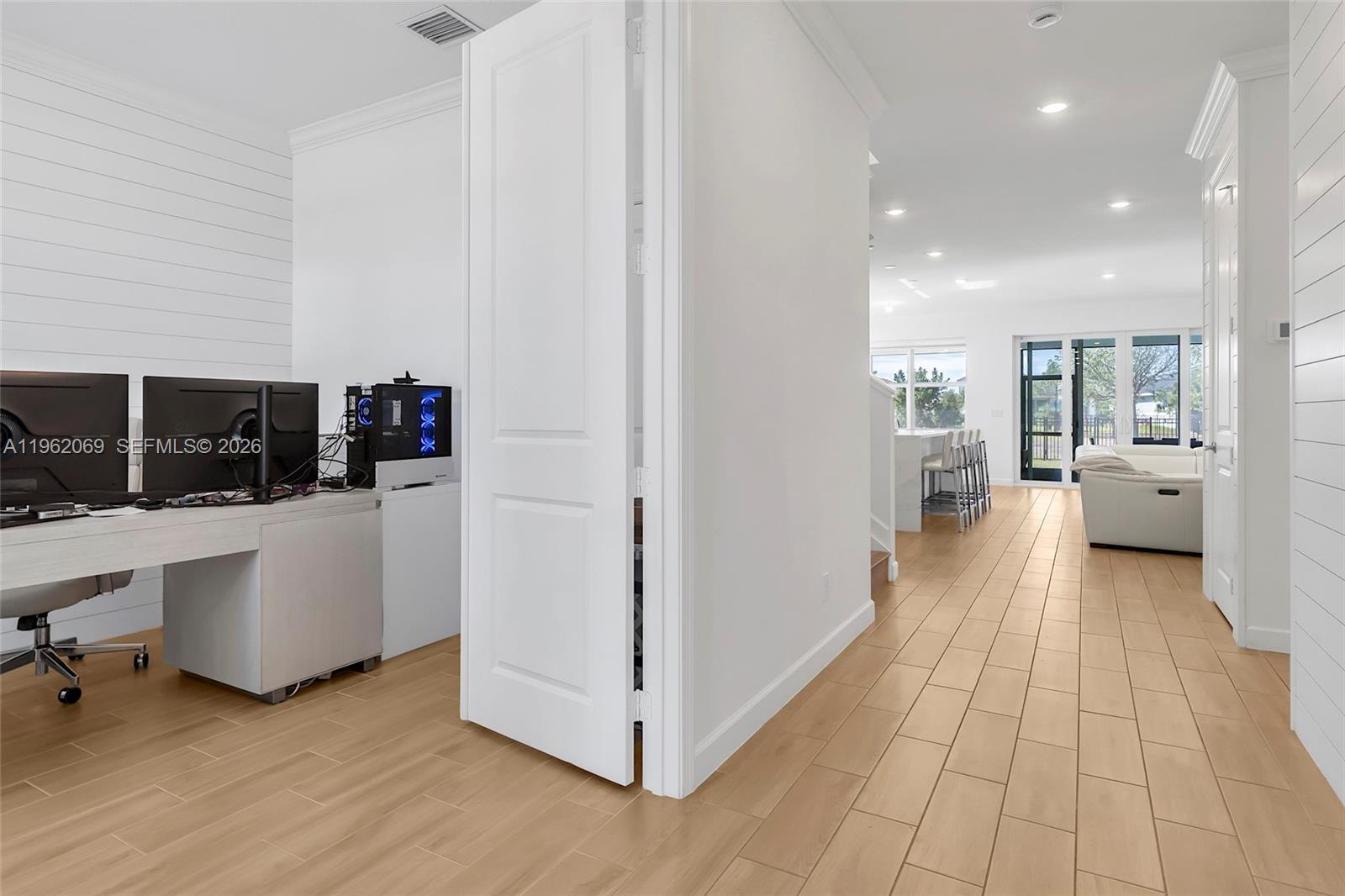 A home office with a computer setup sits beside a hallway leading to a living area — 1600 Wandering Willow Way, Loxahatchee FL 33470, LOXAHATCHEE, FL