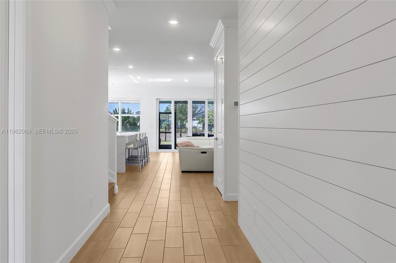 A hallway with light wood flooring leads to an open-concept living area and kitchen — 1600 Wandering Willow Way, Loxahatchee FL 33470, LOXAHATCHEE, FL
