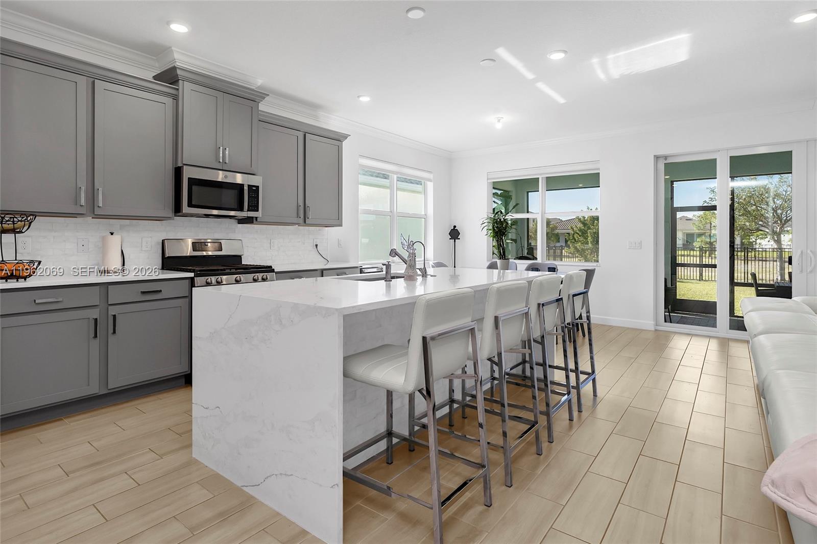 A modern kitchen features gray cabinets, a white marble island, and light wood-look tile flooring — 1600 Wandering Willow Way, Loxahatchee FL 33470, LOXAHATCHEE, FL