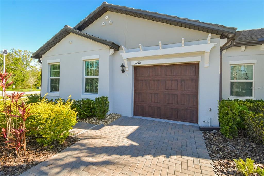 A single-story house exterior features a paved driveway, a brown garage door, and landscaping — 16710 SHELL BAY DRIVE, LAND O LAKES, FL