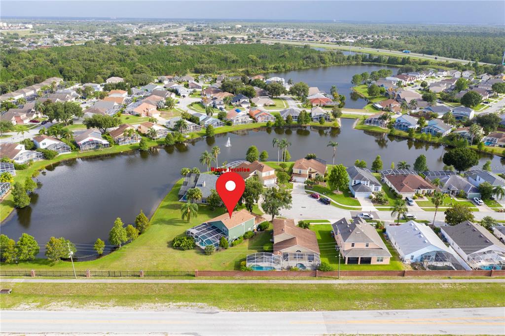 An aerial view shows a green house with a pool cage situated beside a lake — 8051 WHITE CRANE COURT, KISSIMMEE, FL