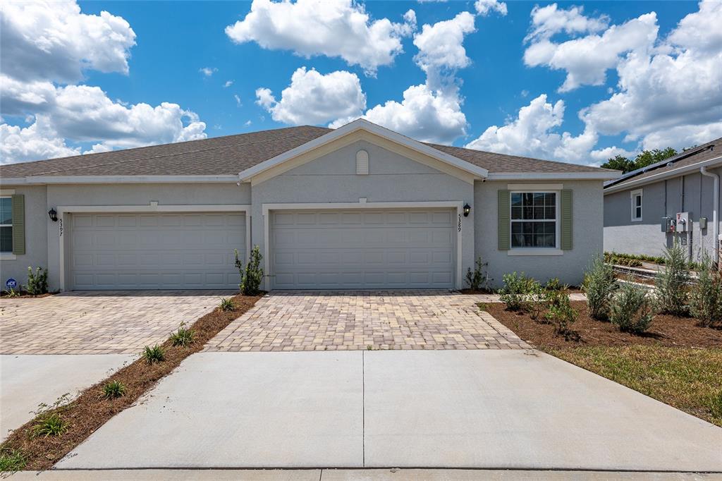 A beige duplex house features two garage doors and a paved driveway under a blue sky — 5389 NW 48TH PLACE, OCALA, FL